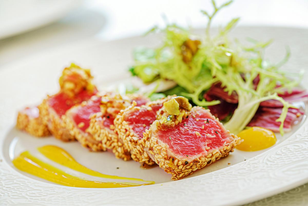 A plate of seared tuna and salad in the background