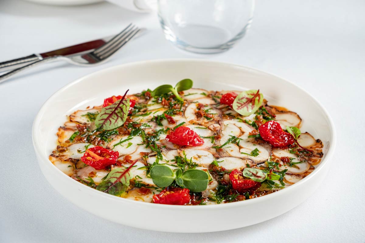 A plate of sliced octopus and various herbs