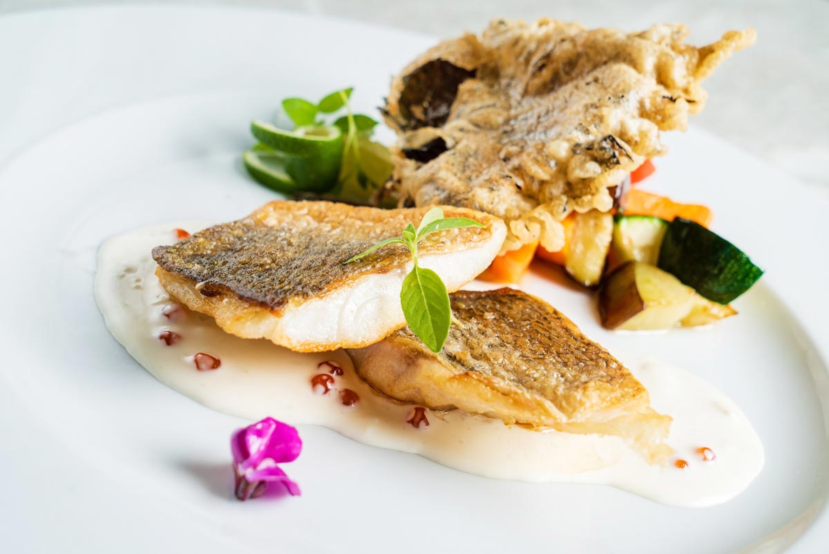 A plate of seared fish with herbs and flowers as garnish