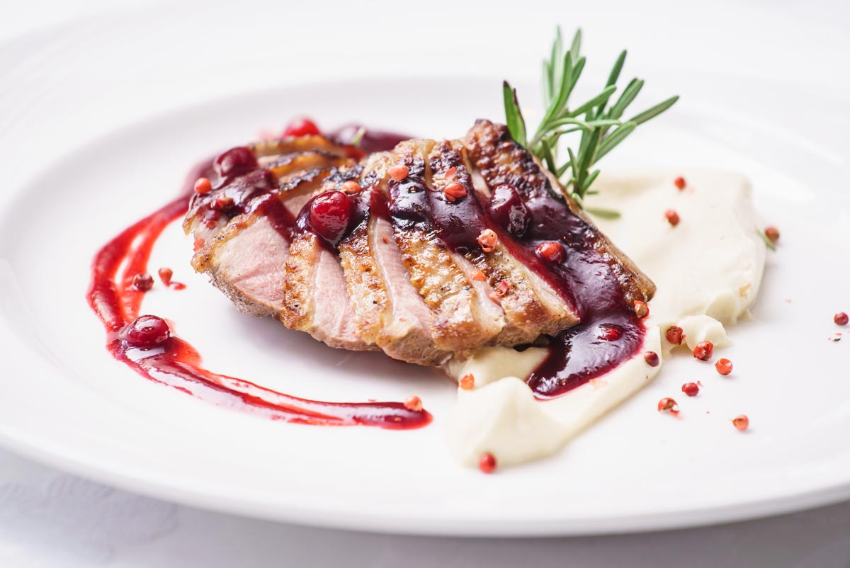 A plate of duck with cranberry sauce on top and rosemary garnish